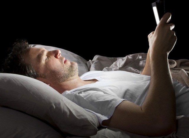 Man laying in bed on phone - best ways to speed up your metabolism 