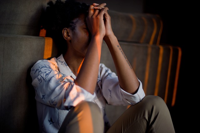 Yound black female sat on the stairs. Her arms and hands are in front of her face, she looks as if she is depressed or sad about something