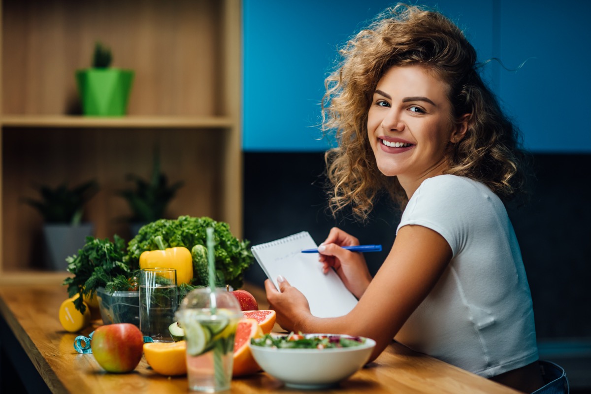 Nutritionist working in office. Doctor writing diet plan on table and using vegetables. Sport trainer