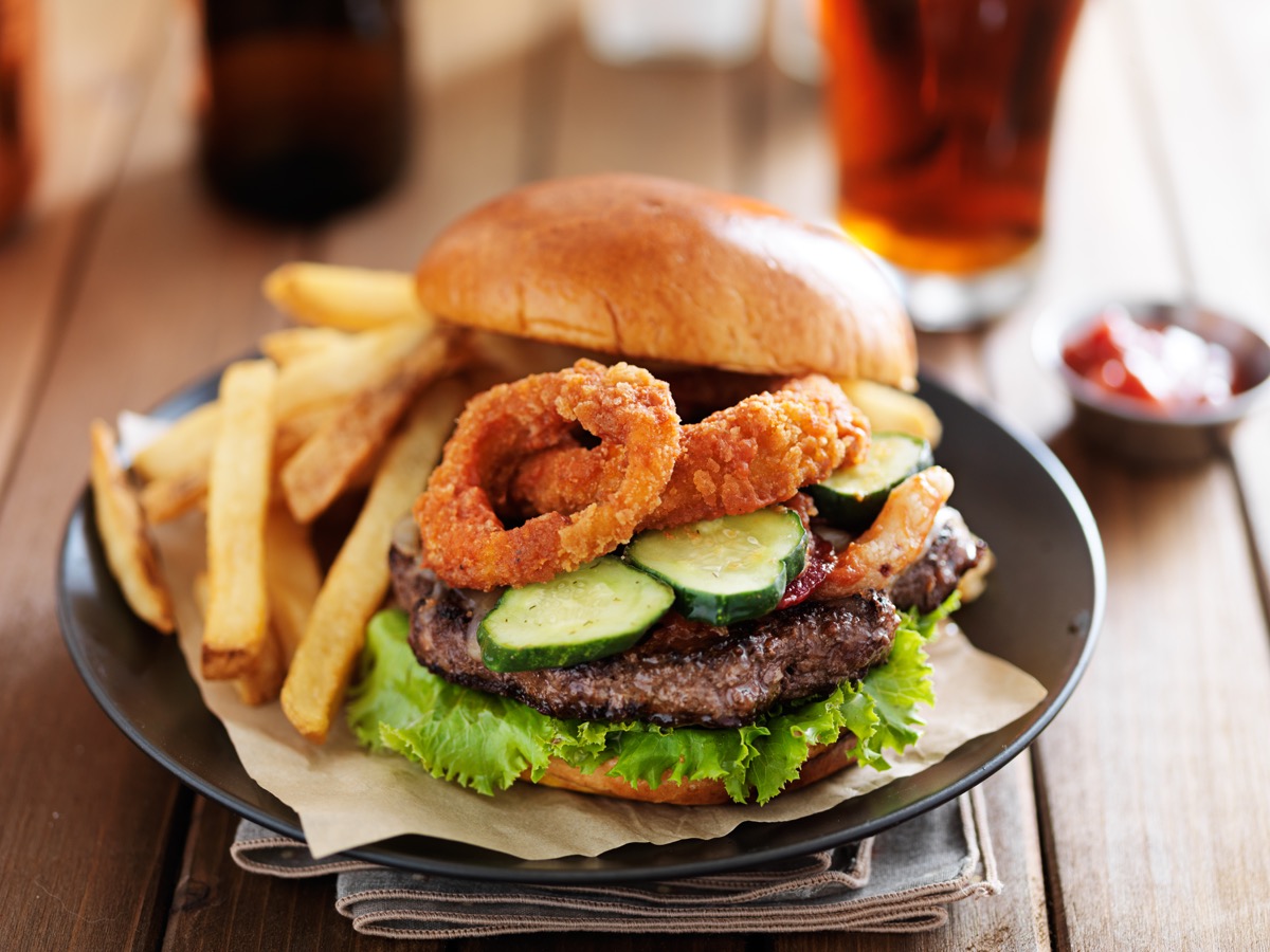 big cheeseburger loaded with onion rings, bacon and bbq sauce served with fries