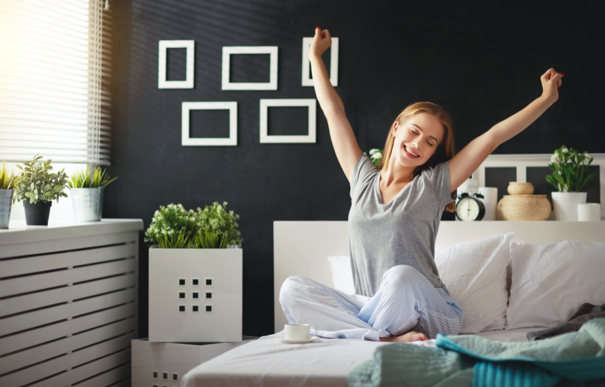 Young happy woman woke up in the morning in the bedroom by the window with her back