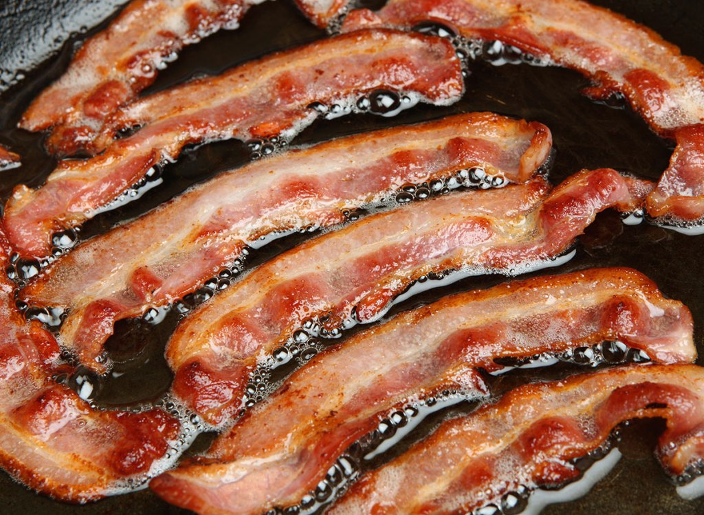 greasy bacon frying in oil in a pan