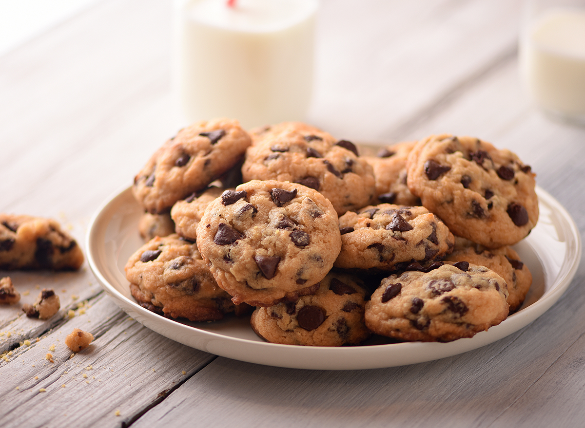 chocolate chip cookies on a plate with two cups of milk in the background