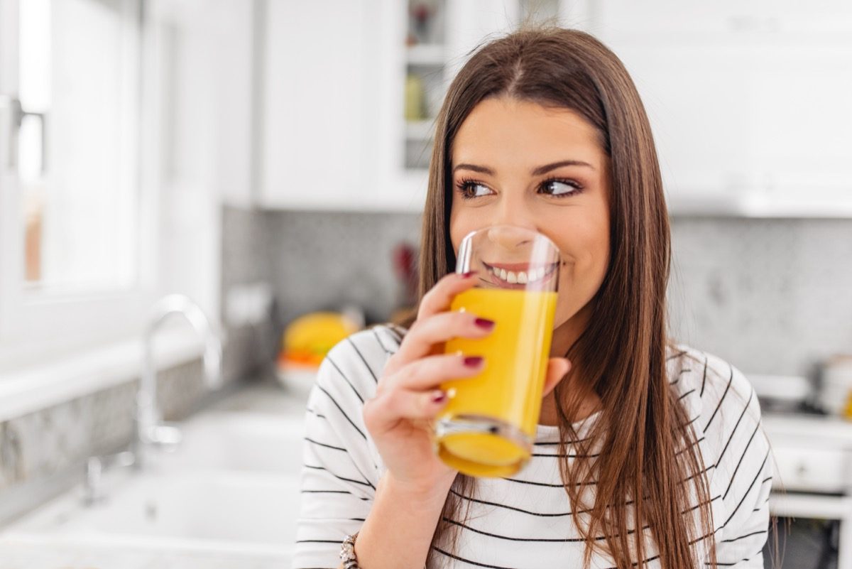 Woman drinking juice while looking through a window.