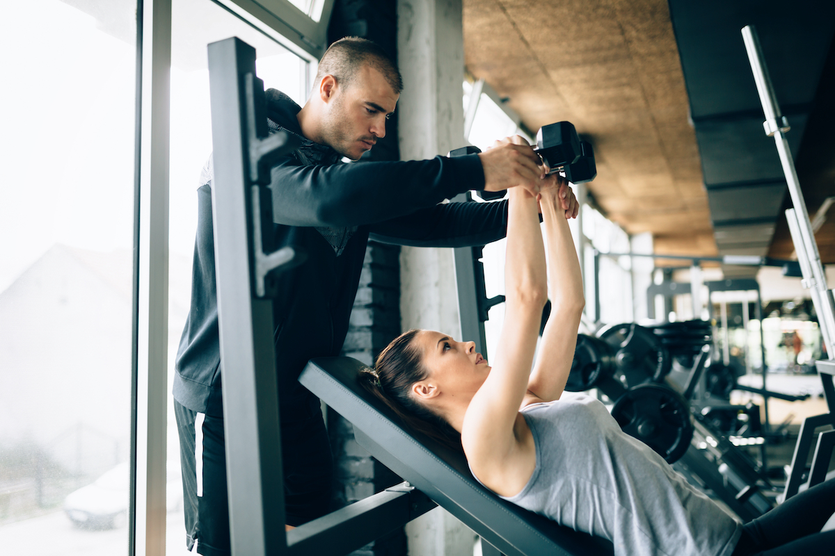 Beautiful woman helped by trainer in gym