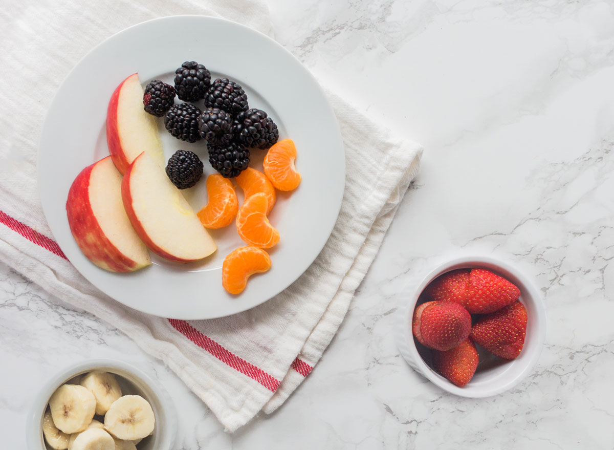 Plate of fruit - apple slices tangerines blackberries - and bowls of strawberries bananas