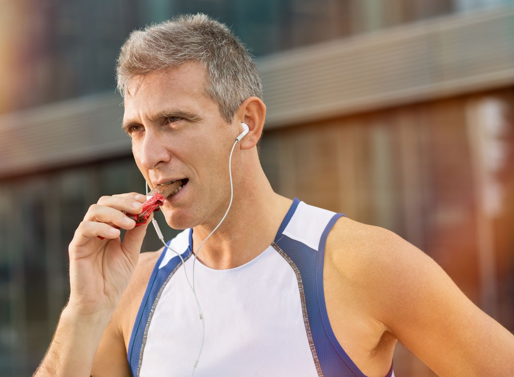 Older male runner eating protein bar