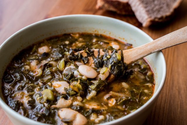 bowl of white bean and kale soup with wooden spoon in it