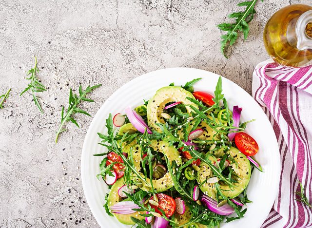 Salad with tomatoes, avocado, arugula, radish, seeds on a bowl