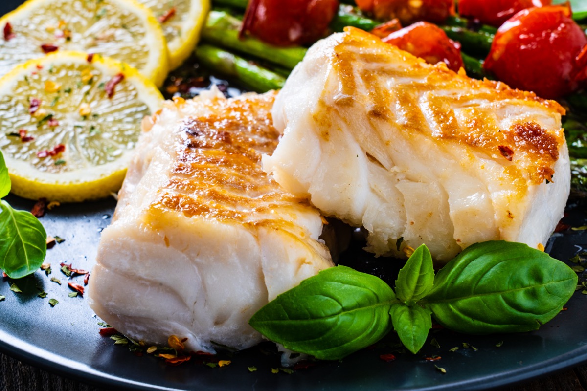 Fried cod fillet with asparagus on wooden table