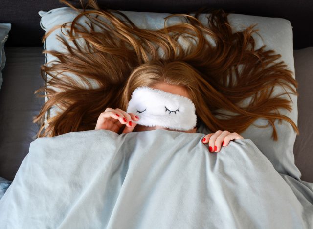 woman wearing fuzzy sleep mask in bed